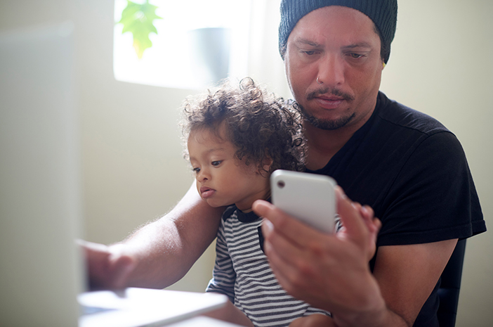 man looking at phone while baby sits on his lap