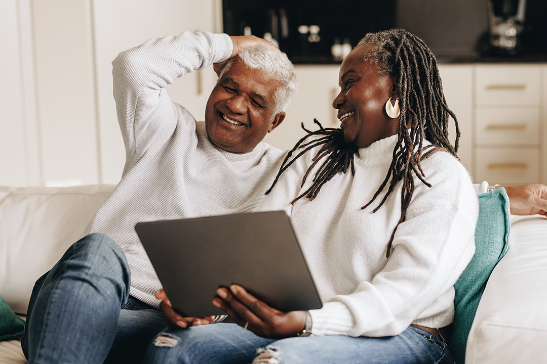 man and woman sitting on couch smiling as woman holds tablet